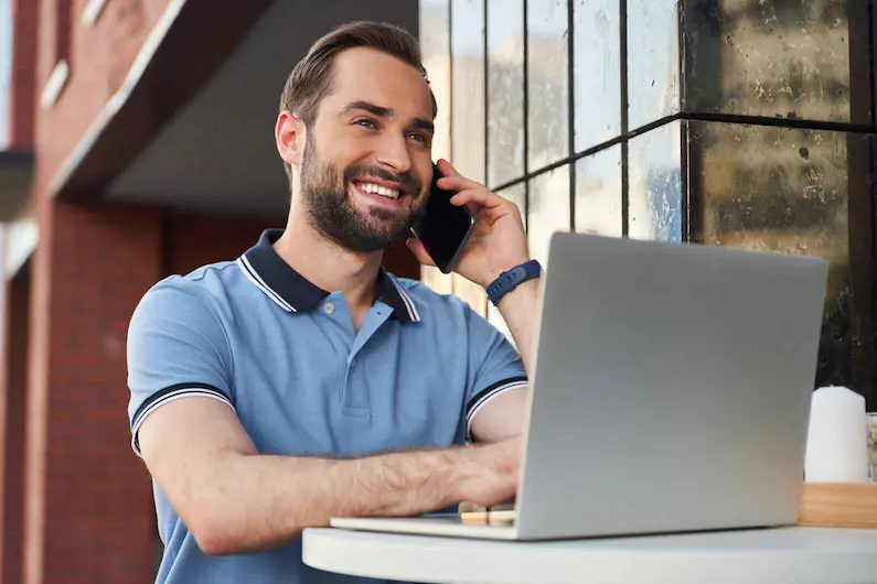 Homme en polo bleu travaillant sur son laptop et téléphone