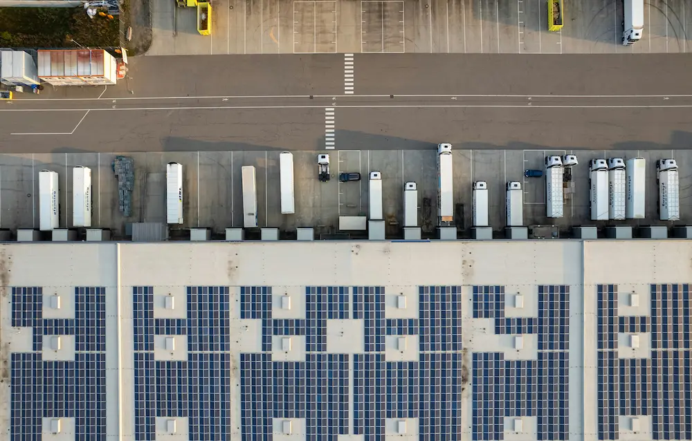 Vue aérienne d'un centre logistique avec camions aux quais de chargement et panneaux solaires